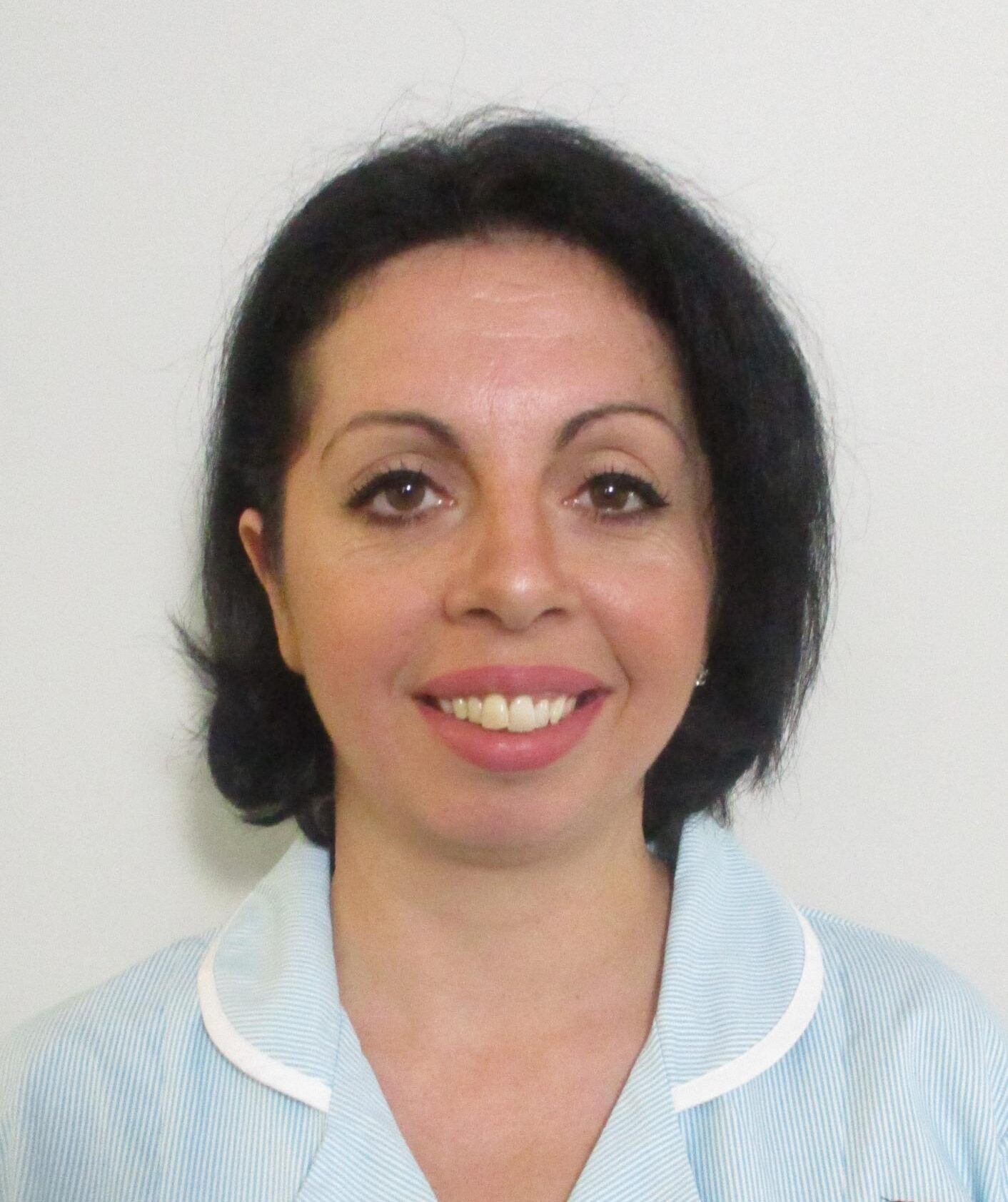 woman with short black hair smiling in light blue nurses uniform