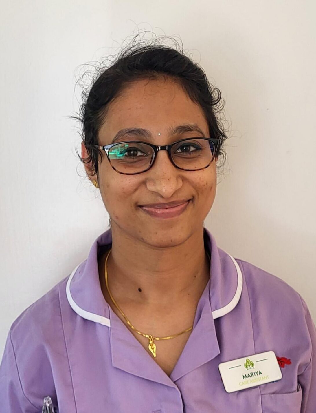 woman with glasses smiling in a lavender nurses uniform